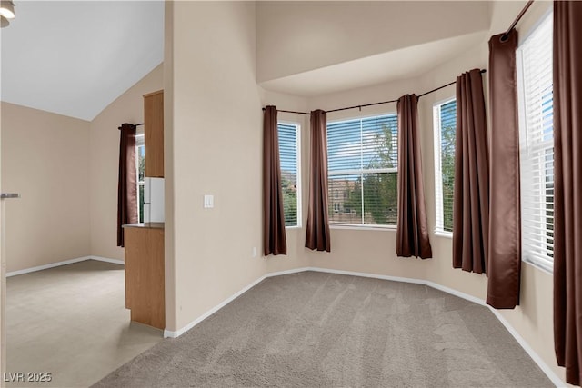 spare room featuring vaulted ceiling, light carpet, and baseboards
