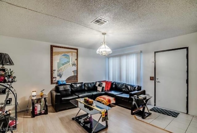 living area featuring light wood finished floors, a textured ceiling, visible vents, and a chandelier