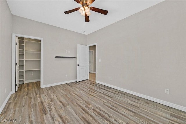 unfurnished bedroom featuring a spacious closet, baseboards, a closet, and wood finished floors