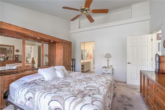 bedroom featuring light colored carpet, a towering ceiling, ensuite bathroom, and a ceiling fan