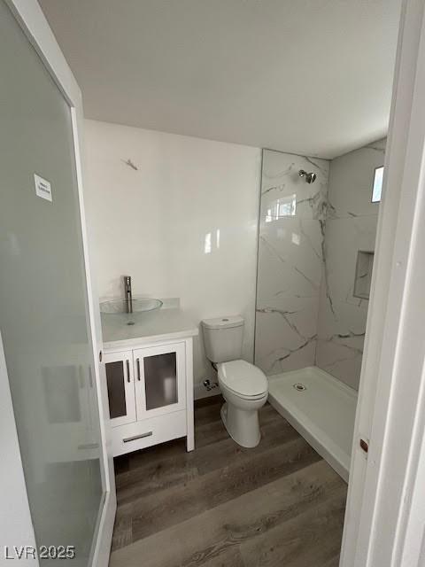 bathroom featuring vanity, toilet, a marble finish shower, and wood finished floors