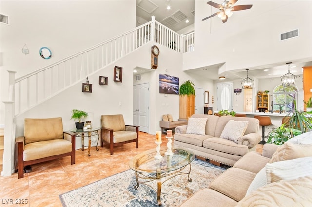 living room featuring a ceiling fan, stairway, visible vents, and a towering ceiling