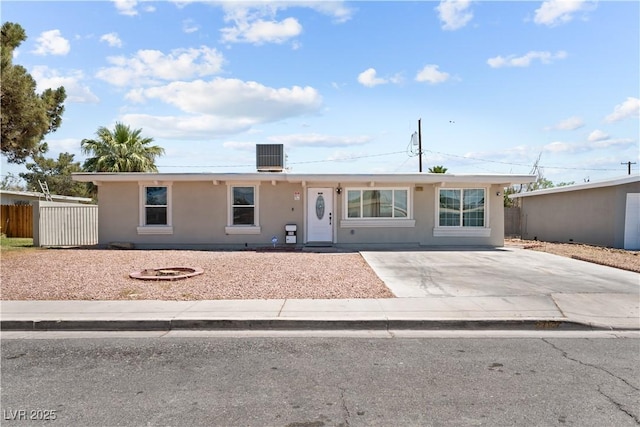ranch-style house featuring central AC unit, driveway, stucco siding, and fence