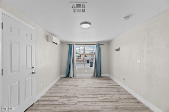 unfurnished room with a wall mounted air conditioner, baseboards, visible vents, and wood finished floors