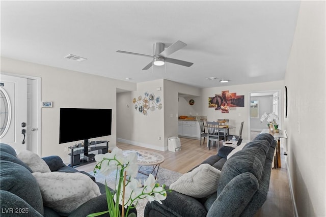 living room featuring a ceiling fan, baseboards, light wood-style flooring, and visible vents