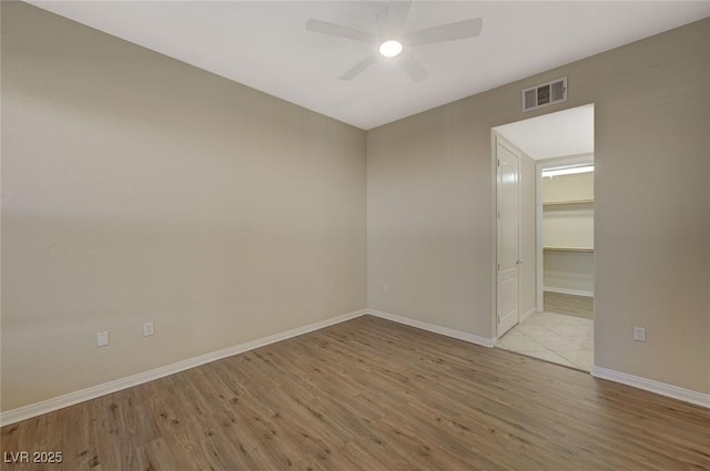 unfurnished room featuring baseboards, visible vents, wood finished floors, and a ceiling fan