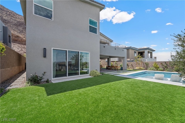 rear view of property with a fenced backyard, a lawn, stucco siding, and a balcony