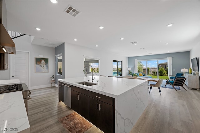 kitchen featuring light wood finished floors, a sink, open floor plan, stainless steel dishwasher, and visible vents