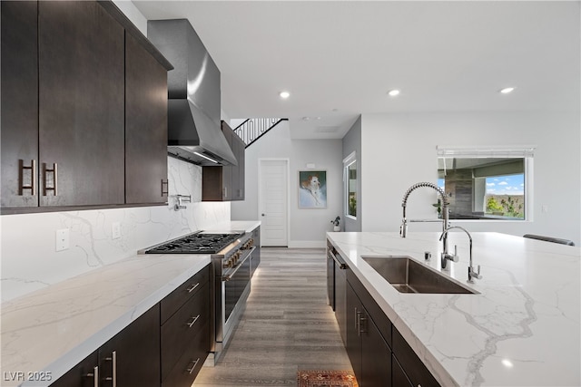 kitchen featuring a sink, wall chimney range hood, high end stainless steel range, wood finished floors, and recessed lighting