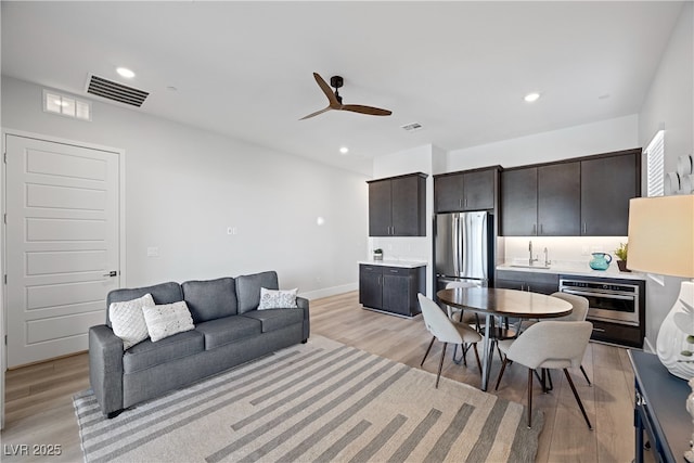 living area featuring light wood-style floors, visible vents, and ceiling fan
