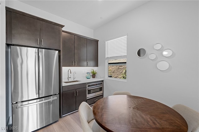 kitchen with a sink, stainless steel appliances, light countertops, dark brown cabinets, and light wood-style floors