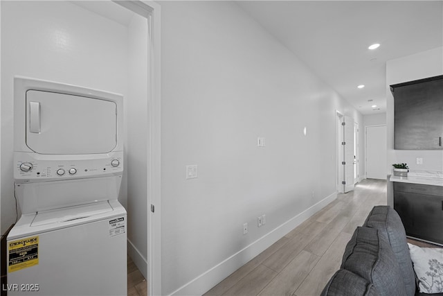clothes washing area with laundry area, stacked washer and dryer, baseboards, and light wood-style floors
