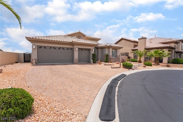 mediterranean / spanish home featuring a tiled roof, decorative driveway, an attached garage, stucco siding, and a gate