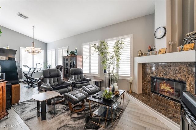 living area featuring a premium fireplace, lofted ceiling, light wood-type flooring, and visible vents