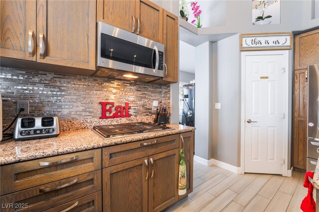 kitchen featuring baseboards, stainless steel appliances, tasteful backsplash, and light stone countertops