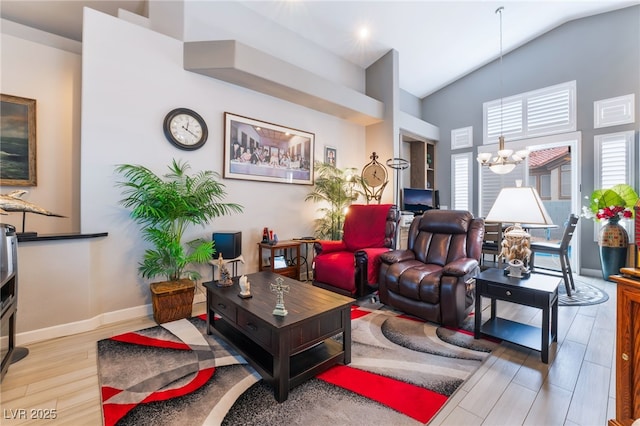 living area with high vaulted ceiling, wood finished floors, baseboards, and a notable chandelier