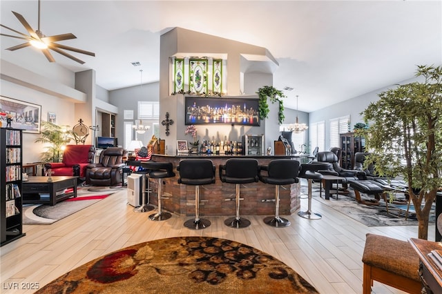 bar with lofted ceiling, ceiling fan with notable chandelier, a bar, and wood finished floors
