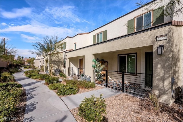 view of side of home featuring stucco siding, a residential view, covered porch, and a gate