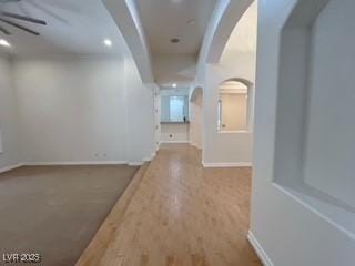 corridor featuring wood finished floors, arched walkways, baseboards, and recessed lighting