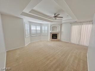 unfurnished living room with a fireplace, ceiling fan, a raised ceiling, and carpet floors