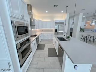 kitchen with a sink, pendant lighting, a large island with sink, light countertops, and appliances with stainless steel finishes