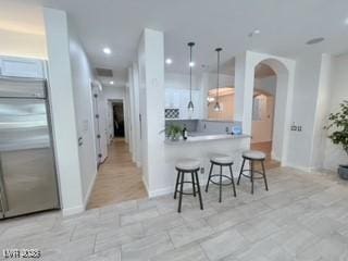 kitchen with a kitchen breakfast bar, recessed lighting, arched walkways, hanging light fixtures, and stainless steel built in fridge