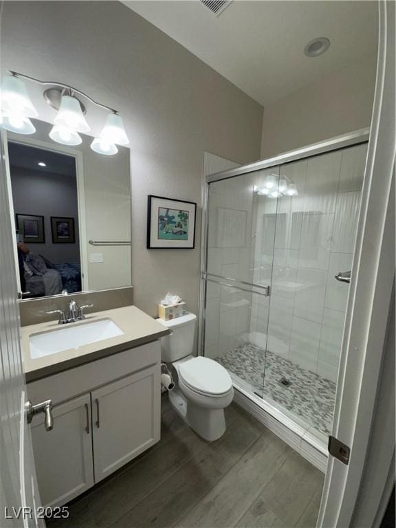 ensuite bathroom featuring toilet, wood finished floors, a stall shower, ensuite bathroom, and vanity
