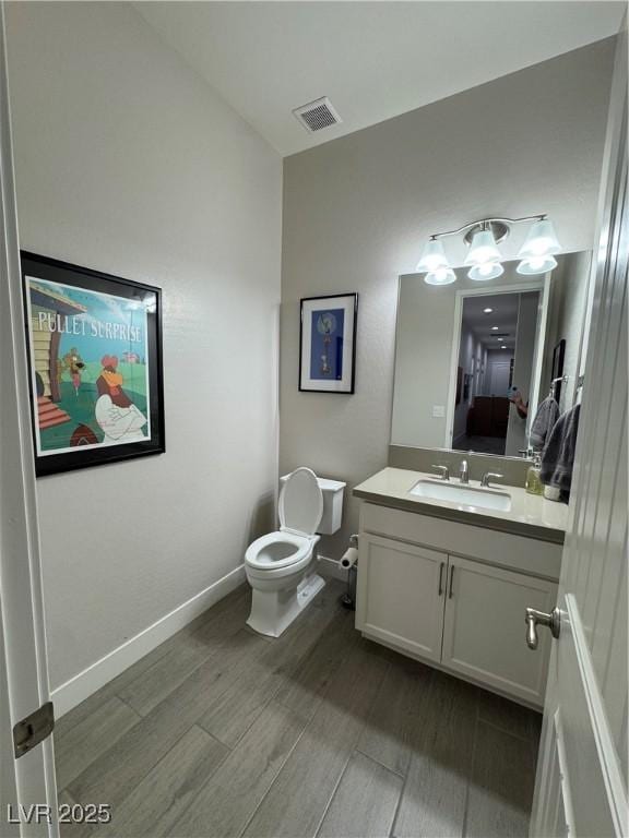 half bathroom featuring toilet, baseboards, visible vents, vanity, and wood finished floors