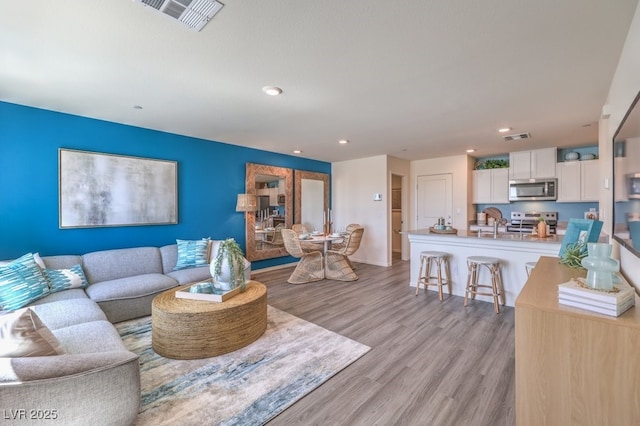 living room with light wood-type flooring, visible vents, and recessed lighting
