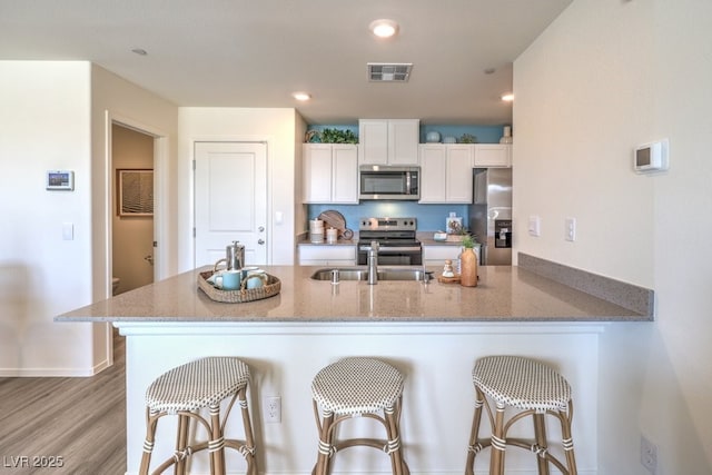 kitchen featuring light stone countertops, white cabinetry, stainless steel appliances, and visible vents
