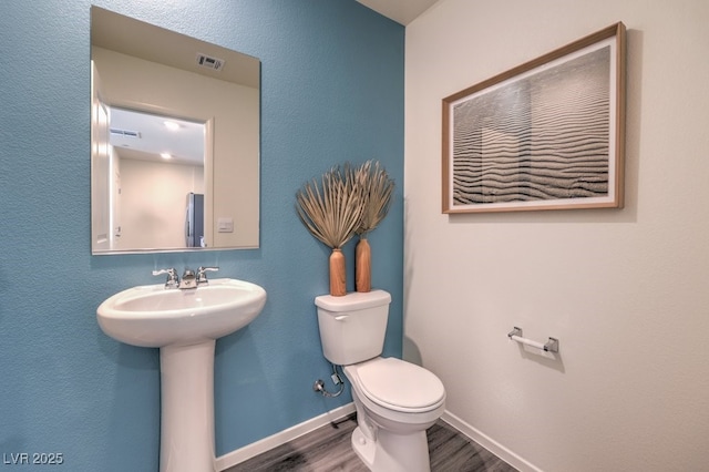 half bathroom featuring toilet, wood finished floors, a sink, visible vents, and baseboards