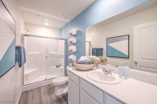 bathroom featuring a shower with door, toilet, visible vents, vanity, and wood finished floors