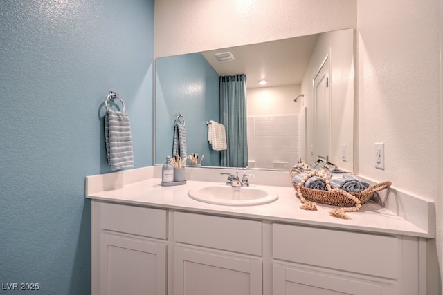 full bathroom with vanity, a textured wall, a shower with curtain, and visible vents