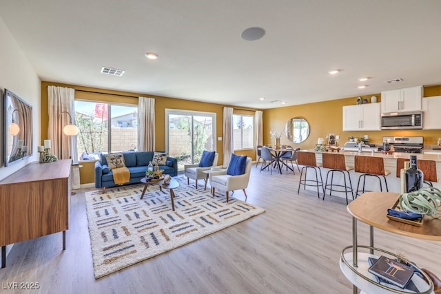 living room with light wood-style floors, visible vents, a healthy amount of sunlight, and recessed lighting