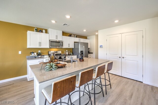 kitchen featuring light wood-type flooring, a sink, white cabinetry, stainless steel appliances, and an island with sink