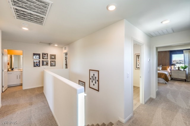 hall featuring baseboards, an upstairs landing, visible vents, and light colored carpet