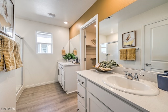 full bath with baseboards, a sink, a shower stall, two vanities, and wood finished floors