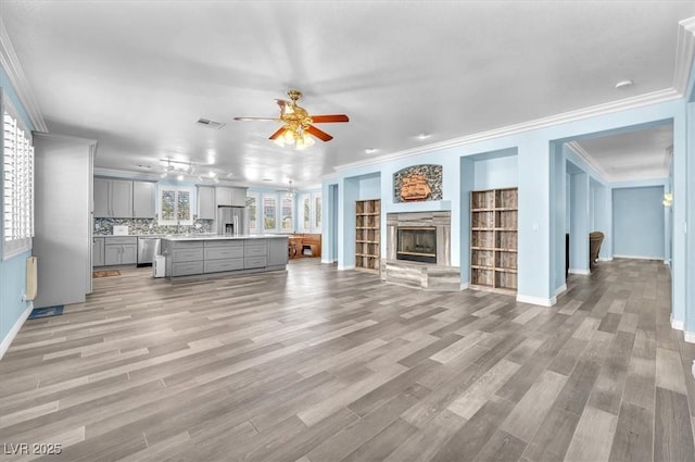 unfurnished living room featuring ornamental molding, ceiling fan, and light wood-style floors