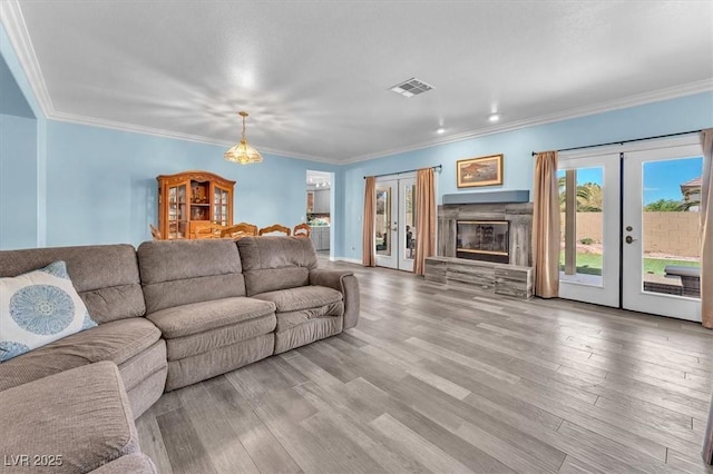 living area with visible vents, french doors, crown molding, and wood finished floors