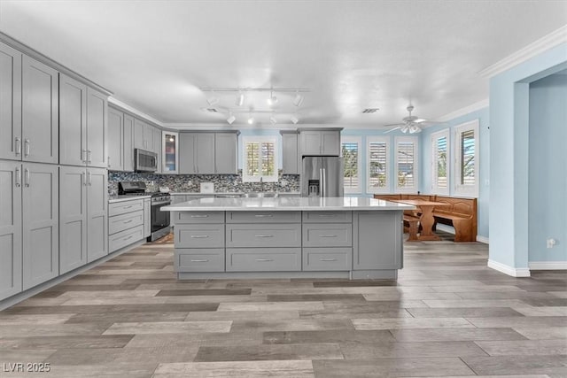 kitchen with crown molding, gray cabinetry, light countertops, and appliances with stainless steel finishes