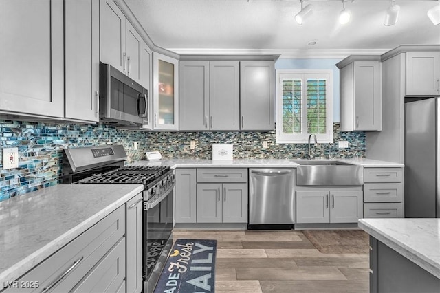 kitchen featuring light wood finished floors, a sink, gray cabinetry, appliances with stainless steel finishes, and light stone counters