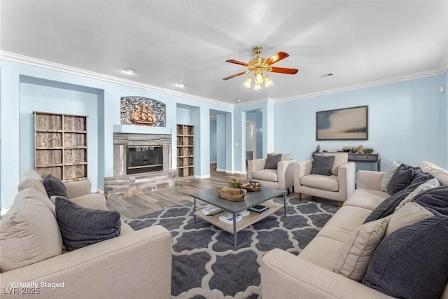 living room with wood finished floors, visible vents, built in features, crown molding, and a ceiling fan