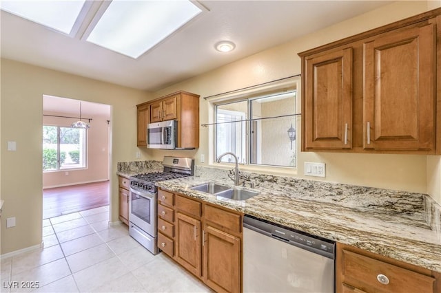 kitchen featuring light tile patterned floors, brown cabinets, a sink, appliances with stainless steel finishes, and light stone counters