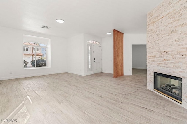 unfurnished living room with baseboards, a stone fireplace, light wood-style flooring, and visible vents