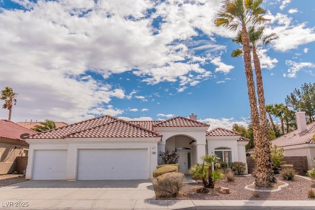 mediterranean / spanish-style home featuring an attached garage, driveway, stucco siding, a tiled roof, and a chimney