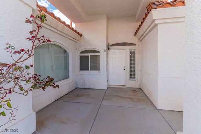 view of exterior entry featuring stucco siding, a tile roof, and a patio