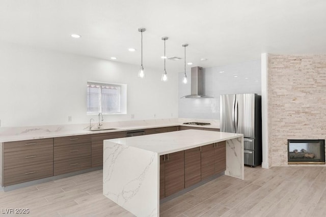 kitchen featuring a sink, stainless steel appliances, wall chimney range hood, and modern cabinets