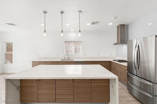kitchen featuring brown cabinetry, visible vents, a sink, wall chimney range hood, and stainless steel appliances
