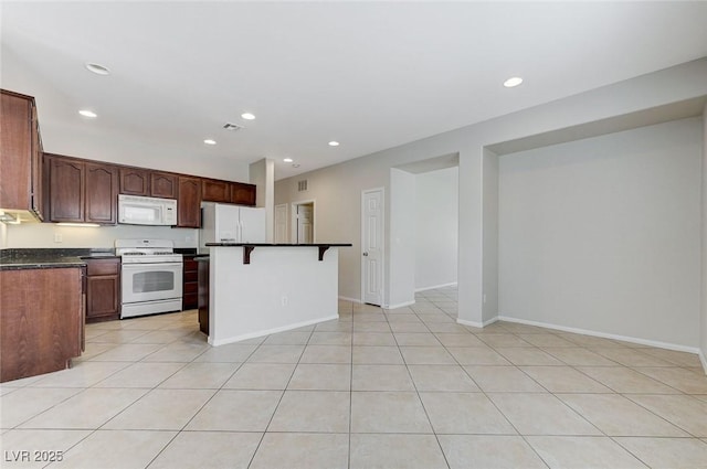 kitchen with a breakfast bar, white appliances, dark countertops, and recessed lighting