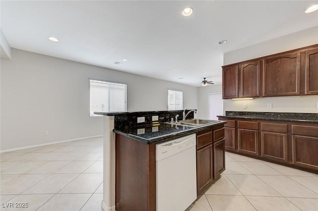 kitchen with dishwasher, light tile patterned floors, ceiling fan, a sink, and dark stone countertops